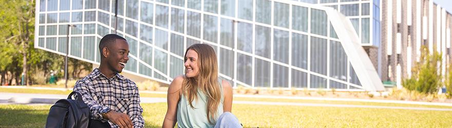 两个学生坐在实验室科学附属楼的草坪上微笑.